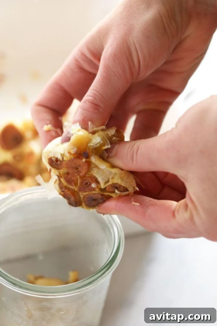 A close-up shot of a hand gently pushing soft, roasted garlic cloves out of their papery skin after roasting, showing their tender texture.