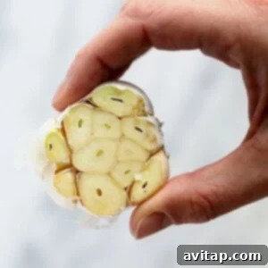 A fresh garlic bulb with the top carefully sliced off, revealing the raw cloves inside.