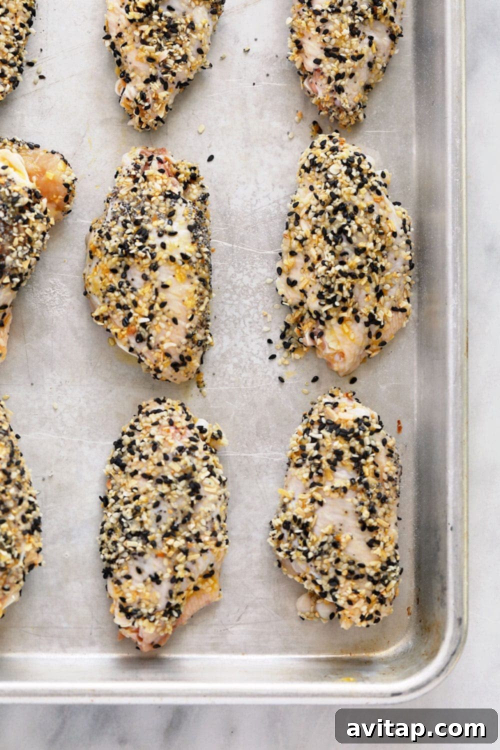 Everything Bagel Seasoning Wings (keto!) Raw chicken wings coated in Everything Bagel Seasoning on a baking sheet, ready for the oven.