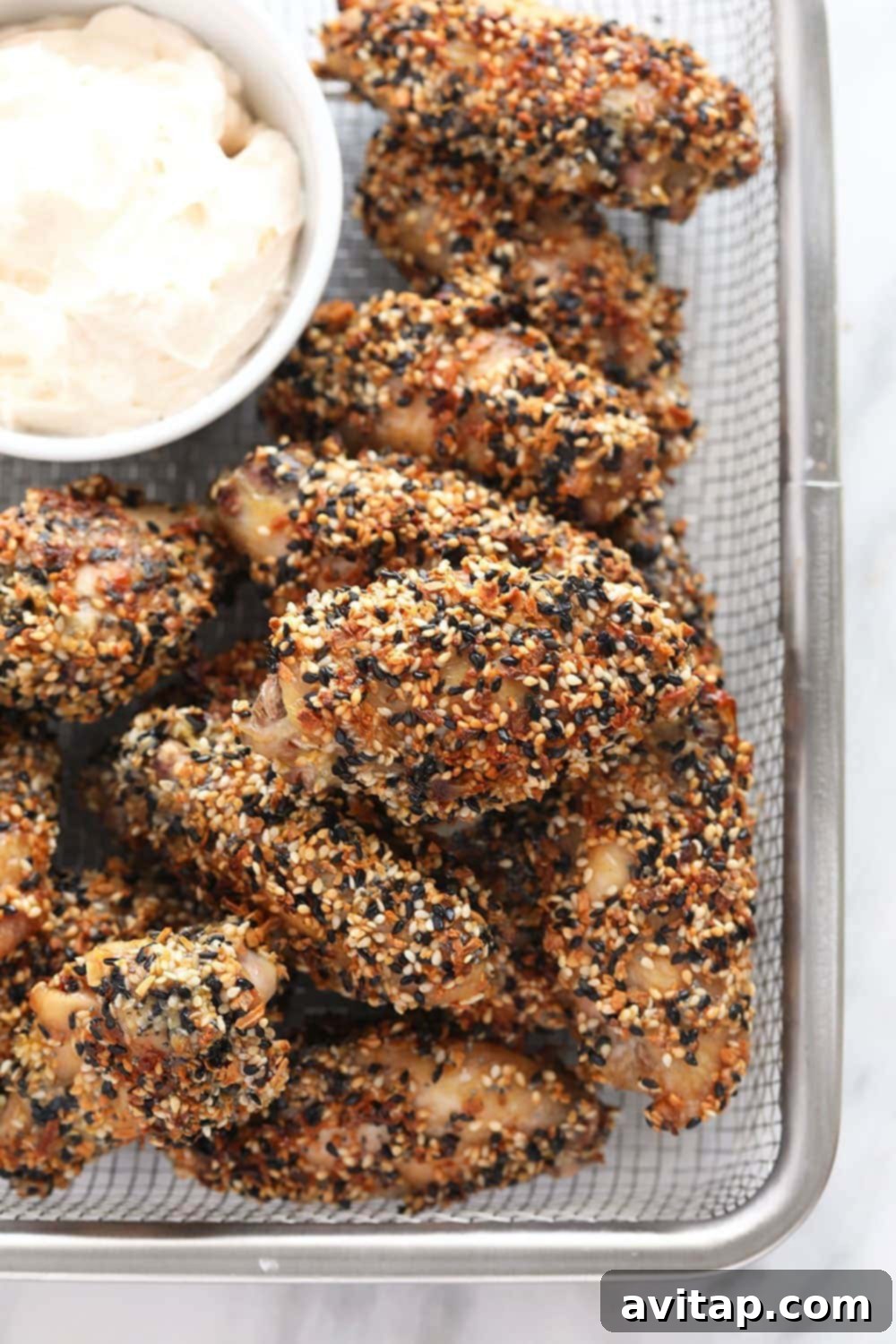Flavorful Crispy Everything Bagel CHICKEN WINGS A serving of crispy Everything Bagel seasoned chicken wings in a rustic basket, with a small bowl of creamy dip on the side.