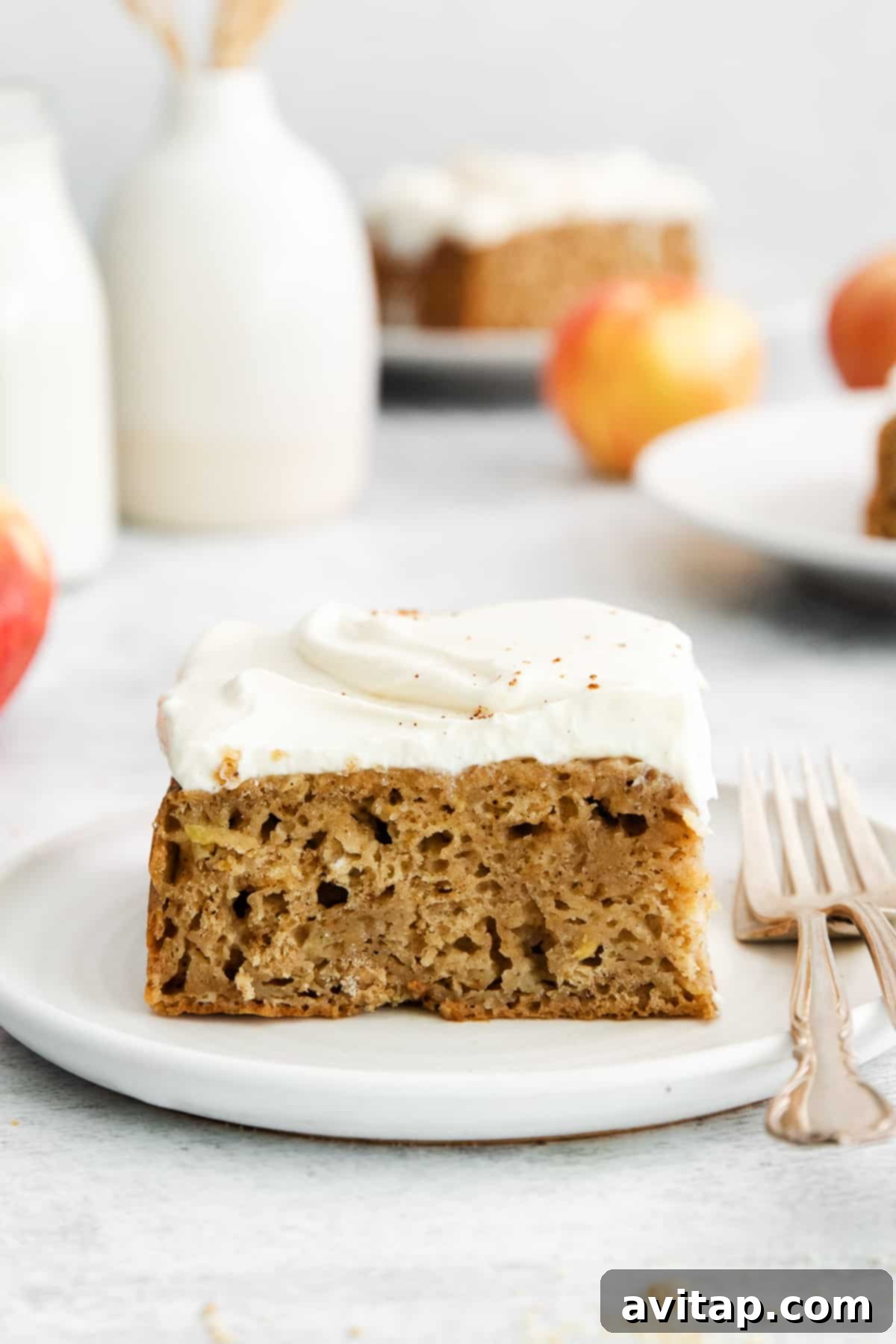 A slice of moist apple cake on a plate, garnished with a light cream cheese frosting.
