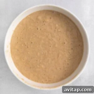 Apple added to the wet ingredients in a bowl.
