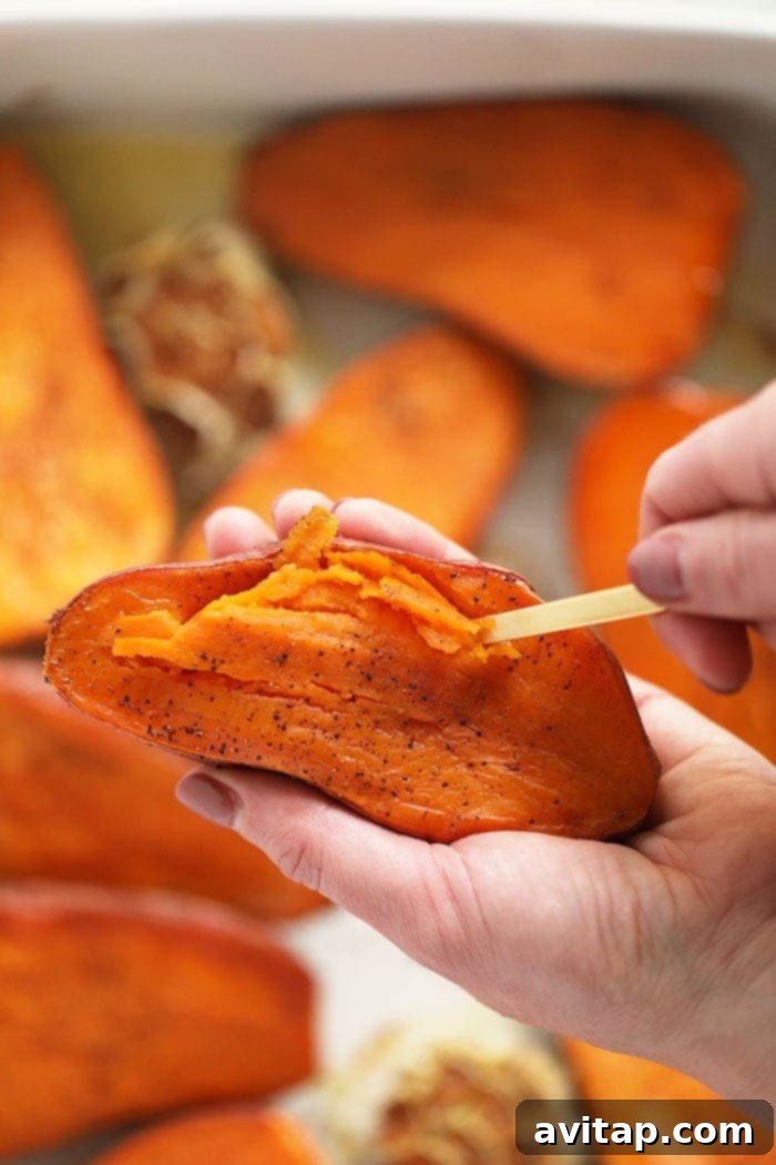 Velvety Sweet Potato Mash 5 A spoon gently scooping the soft, perfectly cooked sweet potato flesh from its skin into a mixing bowl after roasting, alongside the roasted garlic.