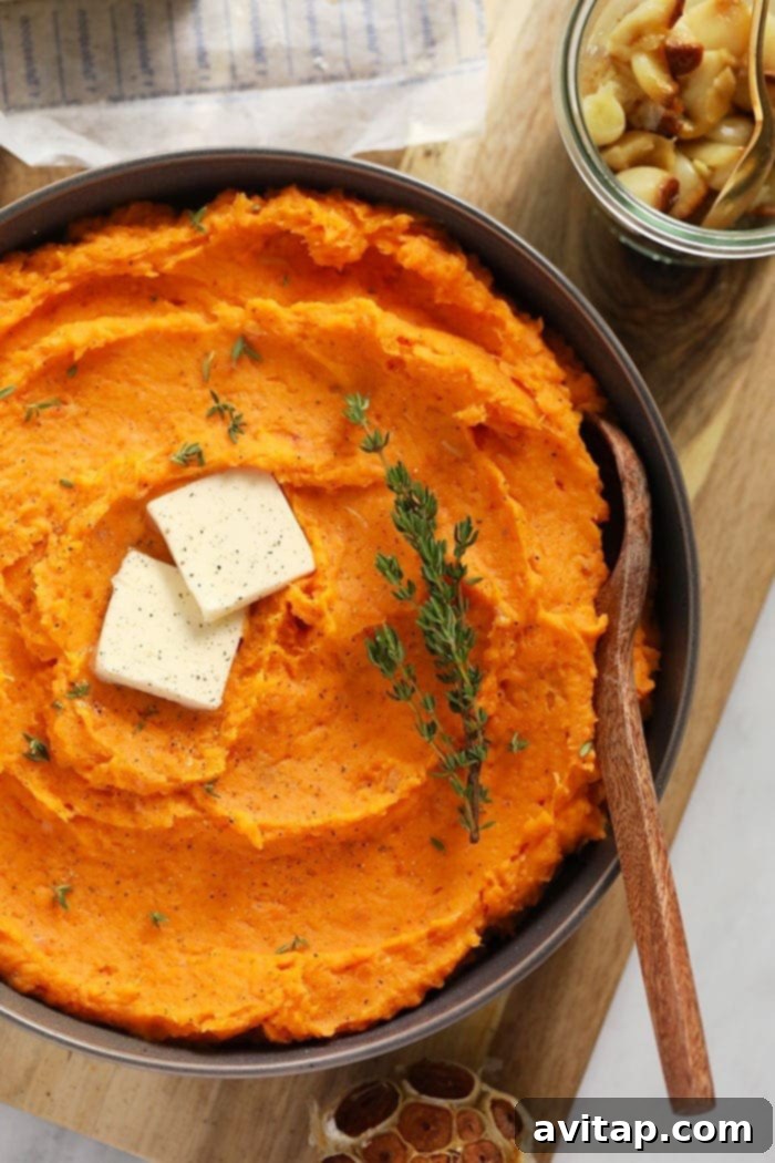 Velvety Sweet Potato Mash 6 A beautifully presented bowl of creamy mashed sweet potatoes, topped with a generous dollop of melted butter and garnished with fresh thyme leaves, ready to be enjoyed.