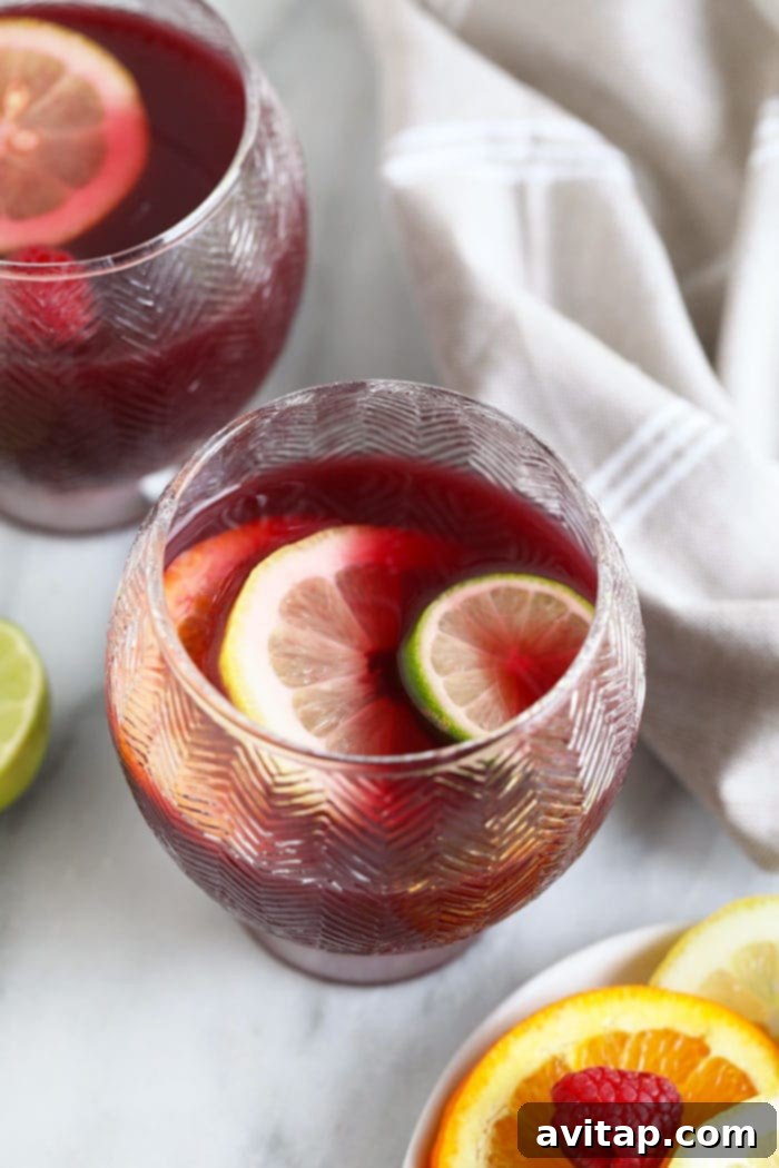 A glass of easy red wine sangria filled with sliced oranges, apples, and berries.