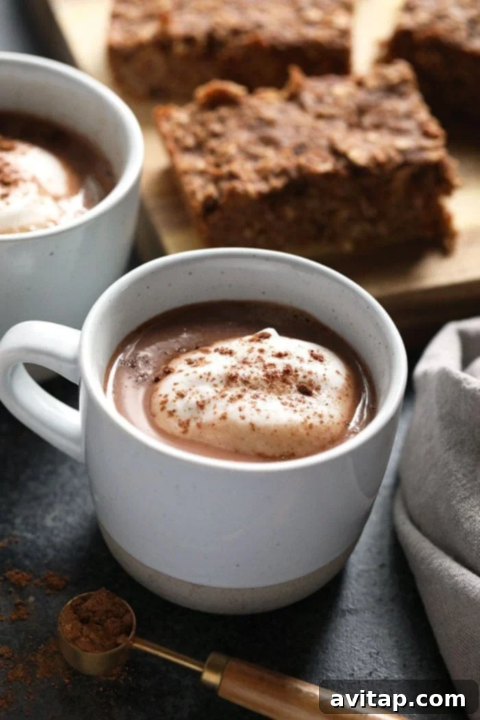 A mug of vegan chai hot chocolate, topped with whipped cream and a dusting of cinnamon, against a cozy background.