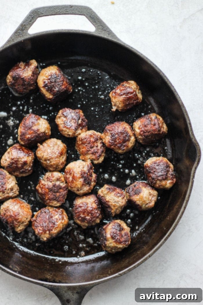 Sear these Italian meatballs for a delicious crunchy outer shell and enhanced flavor before simmering in sauce. Golden-brown Italian meatballs sizzling in a cast iron skillet, ready to be simmered in sauce.
