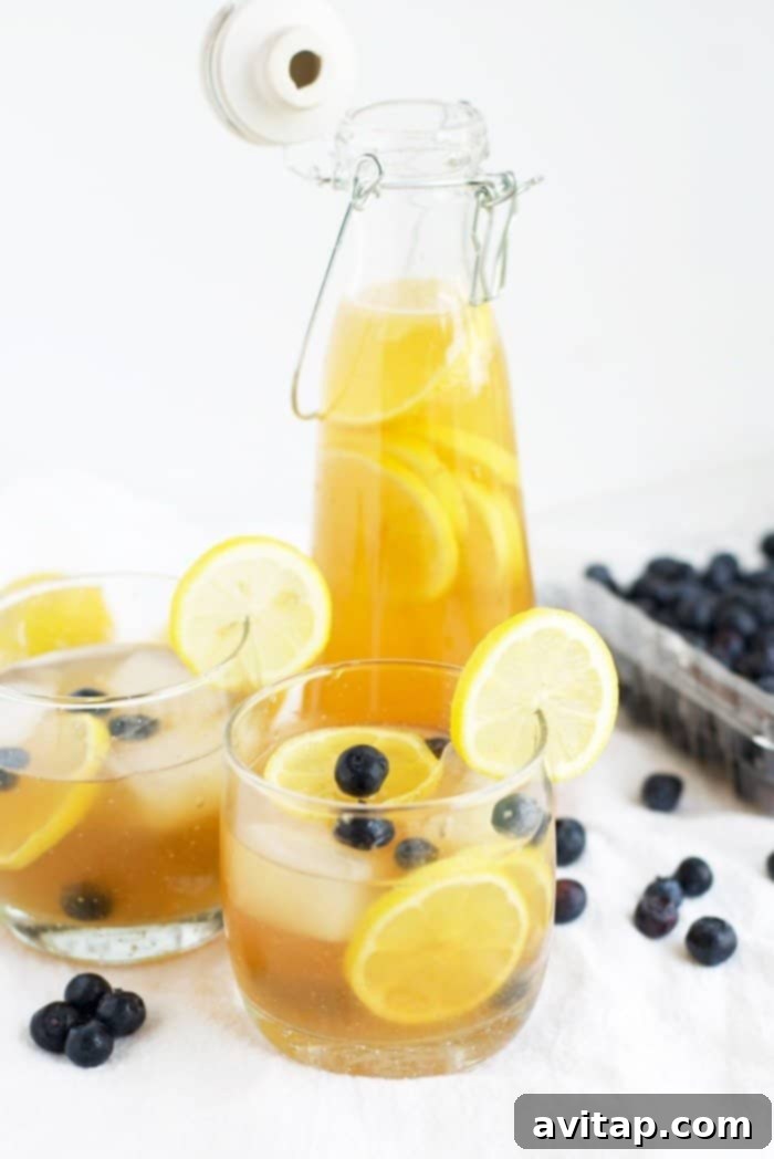 Two glasses of Kombucha Lemonade garnished with blueberries and lemon slices, alongside a pitcher of the drink, ready to be served.