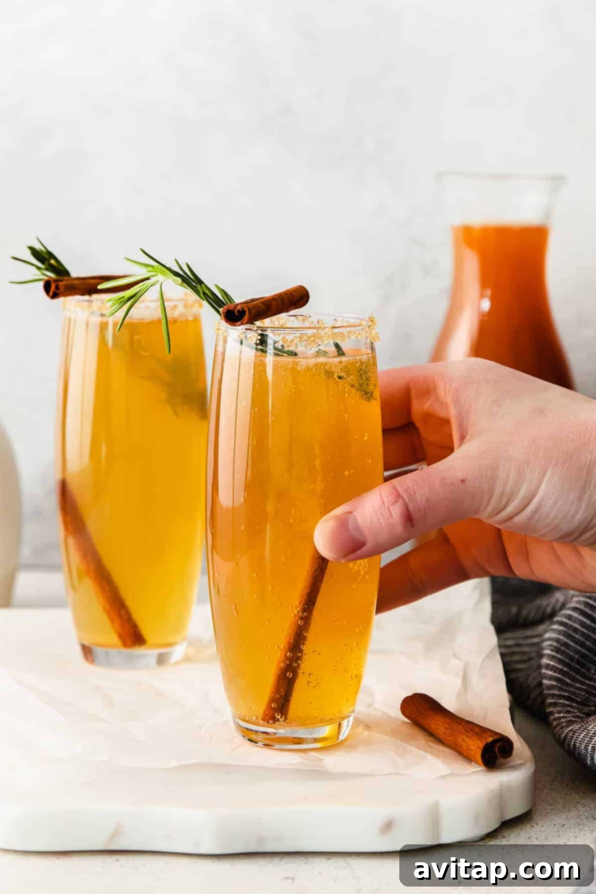 Autumn Apple Mimosa 2 A hand holding a perfectly garnished Apple Cider Mimosa, showcasing its festive appeal.