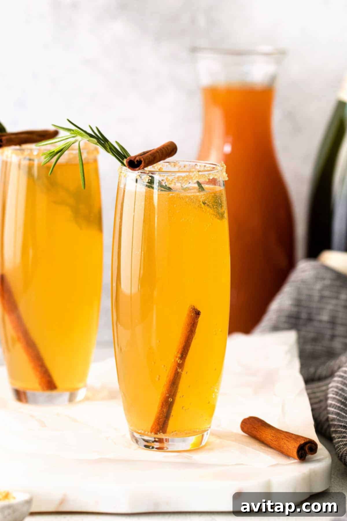 Autumn Apple Mimosa 8 An Apple Cider Mimosa garnished with cinnamon sticks and a rosemary sprig, on a rustic background.