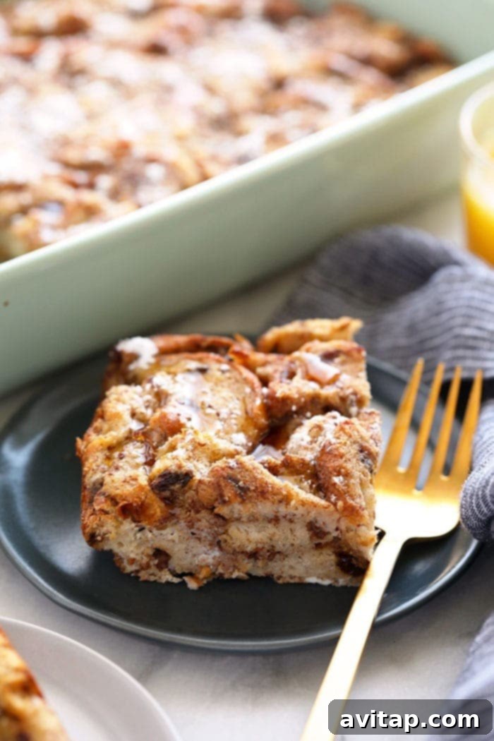 A golden-brown Cinnamon French Toast Bake served on a white plate, drizzled with syrup and powdered sugar.