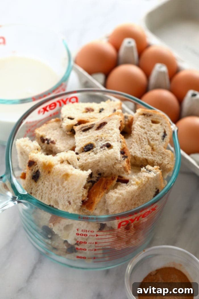 Slices of cinnamon raisin bread cut into cubes, ready for a French toast bake in a measuring cup.