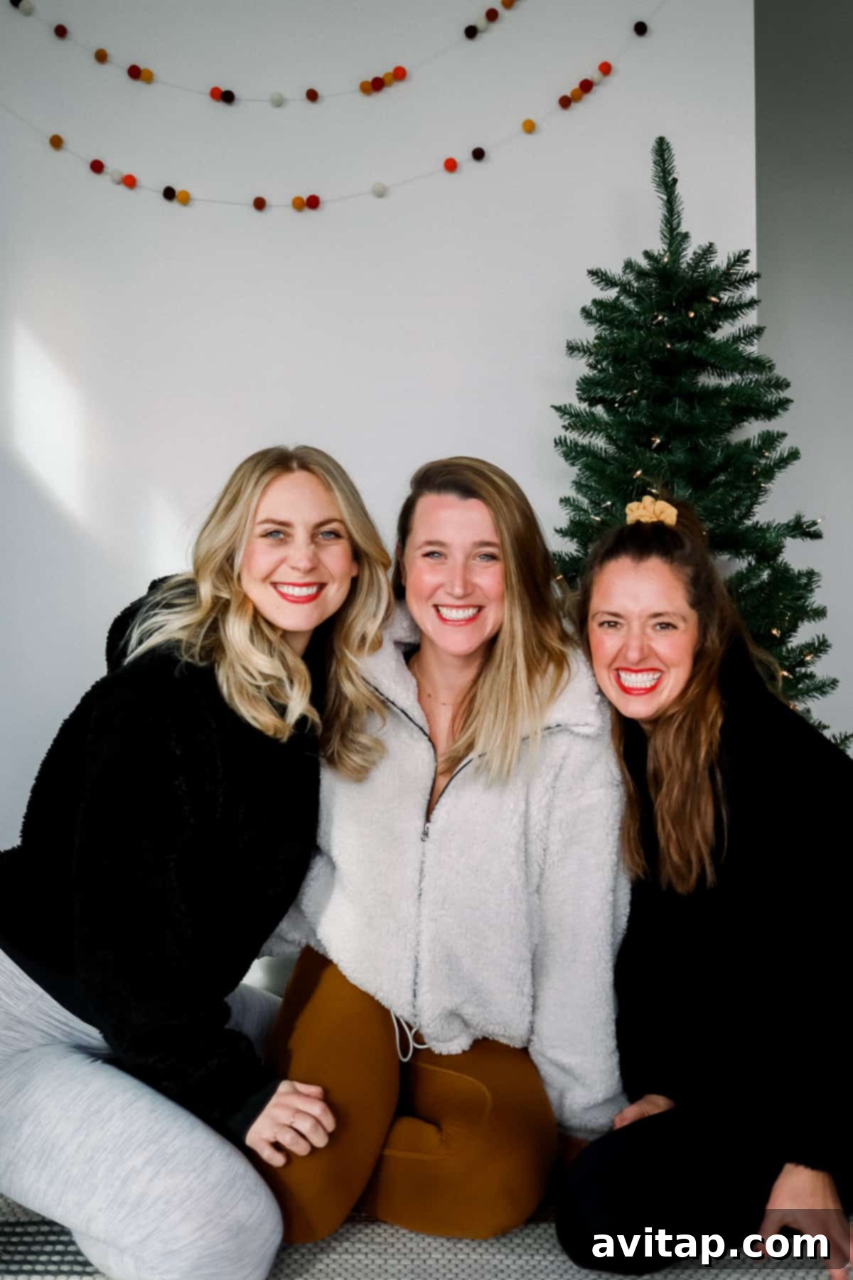 Three women sitting comfortably in Lululemon apparel in front of a festive Christmas tree, showcasing holiday cheer and cozy styles.
