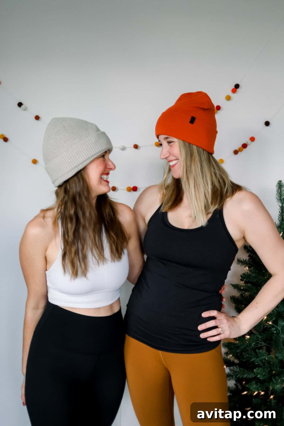 Two women smiling, dressed in Lululemon workout gear and festive stocking caps, in front of a Christmas tree.