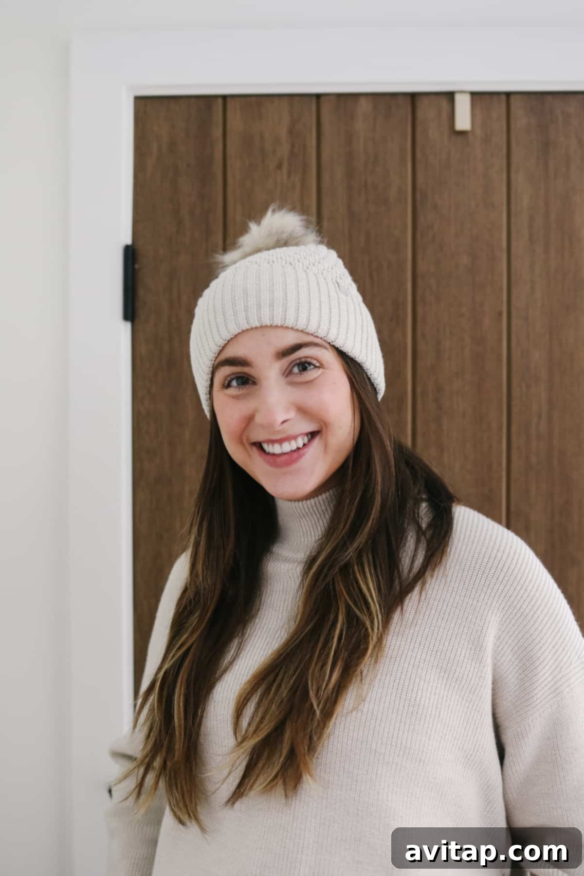 A smiling woman wearing a stylish beige Lululemon Bubble Knit Pom Beanie.