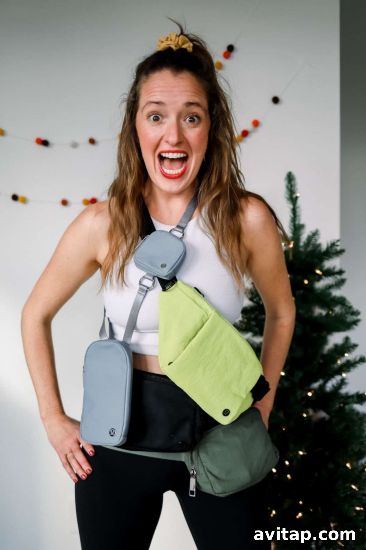A cheerful woman playfully modeling three different Lululemon fanny packs, showcasing various styles and sizes.