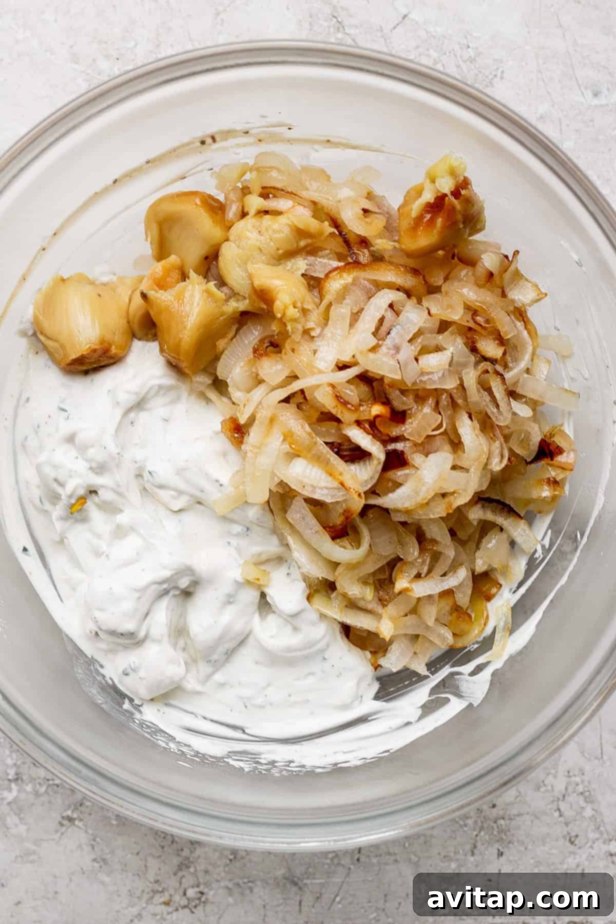 Irresistible Caramelized Onion Dip 2 A bowl contains beautifully roasted garlic cloves, golden caramelized onions, and a creamy, herb-infused dip base, showcasing the key components before mixing.