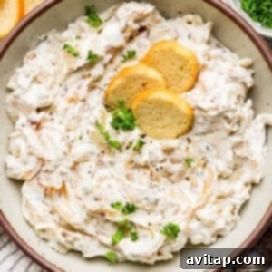 A bowl of creamy dip topped with fresh herbs and three round crackers.