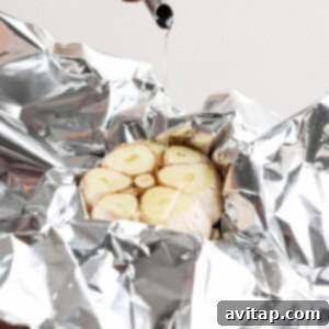 Oil being poured onto a halved garlic bulb placed on aluminum foil, ready for roasting to sweet perfection.