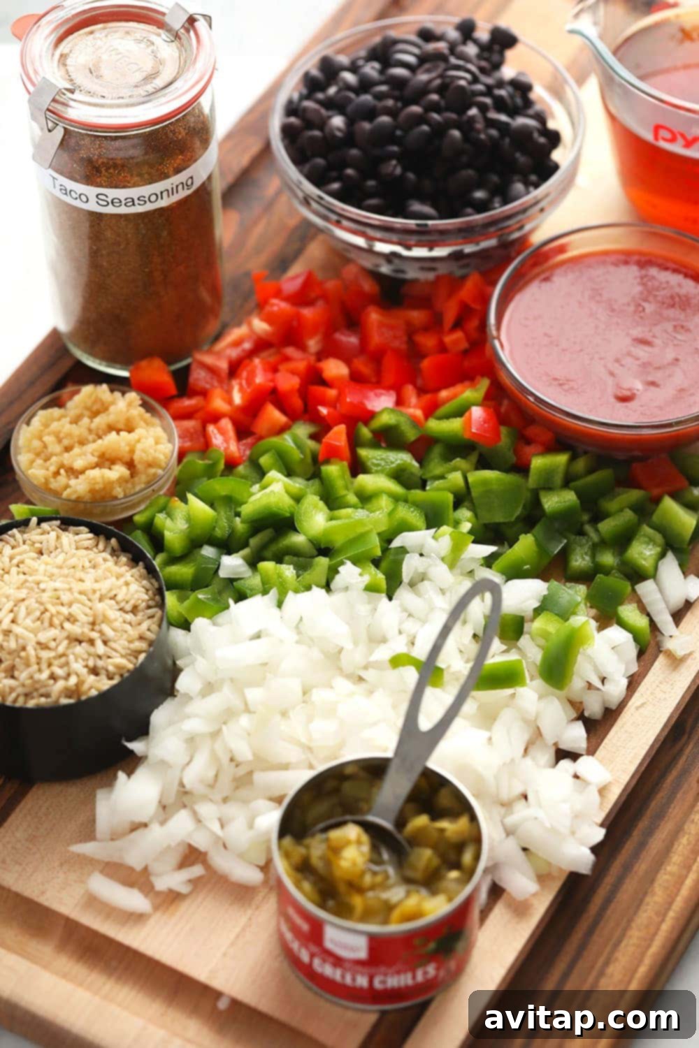 Fresh ingredients for Mexican ground beef skillet laid out on a wooden cutting board, including bell peppers, onion, garlic, and seasoning.