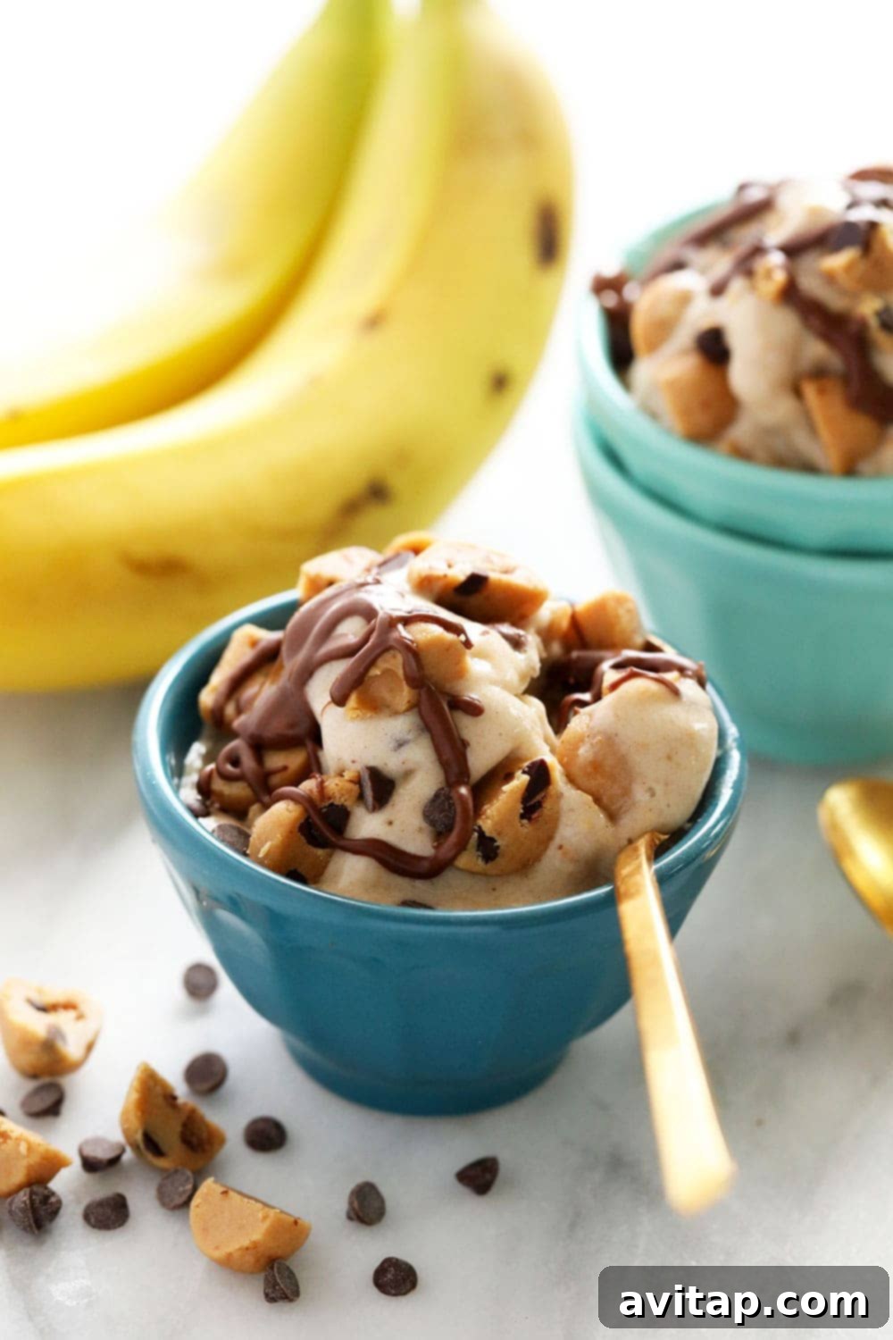 A bowl of creamy vegan cookie dough banana nice cream, topped with extra cookie dough chunks and a drizzle of chocolate sauce.