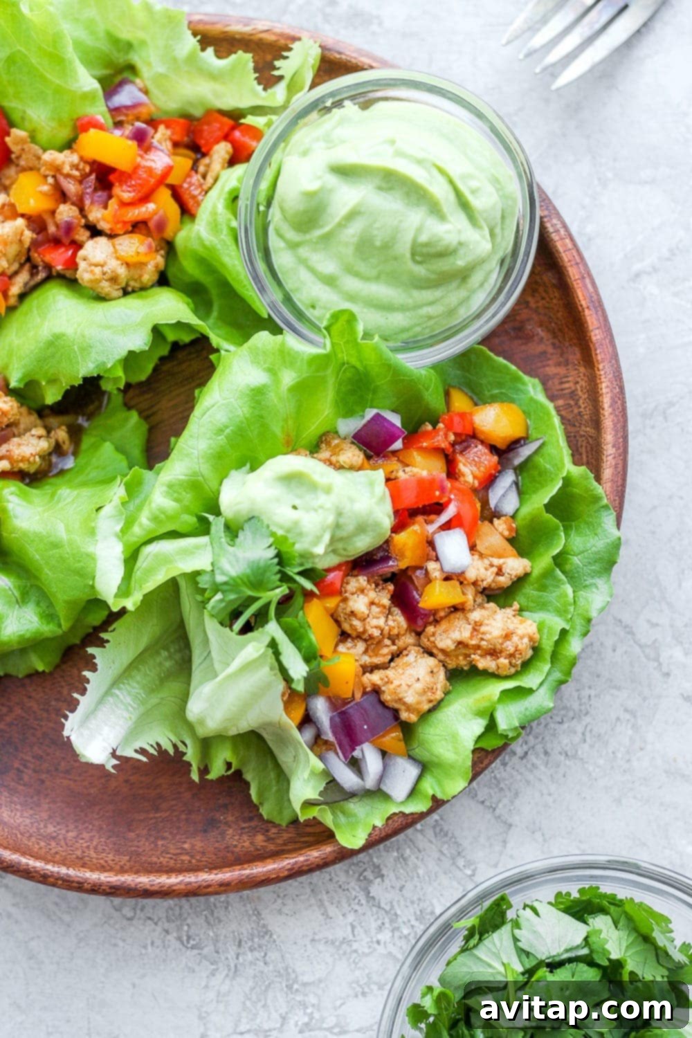 Two fajita ground turkey lettuce wraps on a plate, drizzled with avocado crema