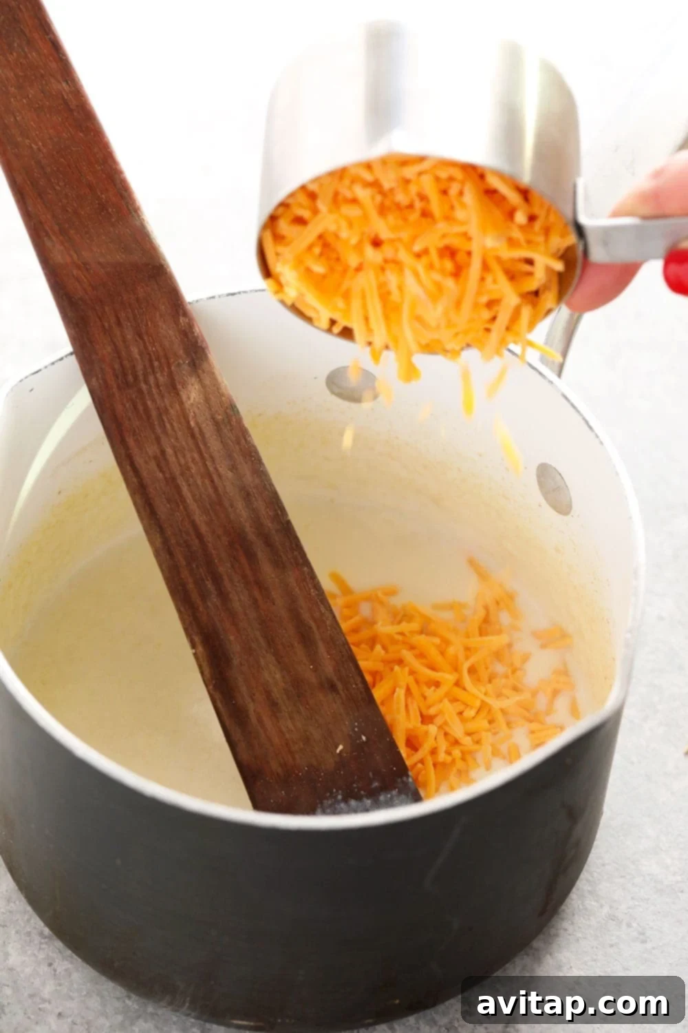 Ultimate Triple Cheese Cauliflower Mac 3 Close-up of a person mixing the creamy, golden cheese sauce in a pot on the stovetop.