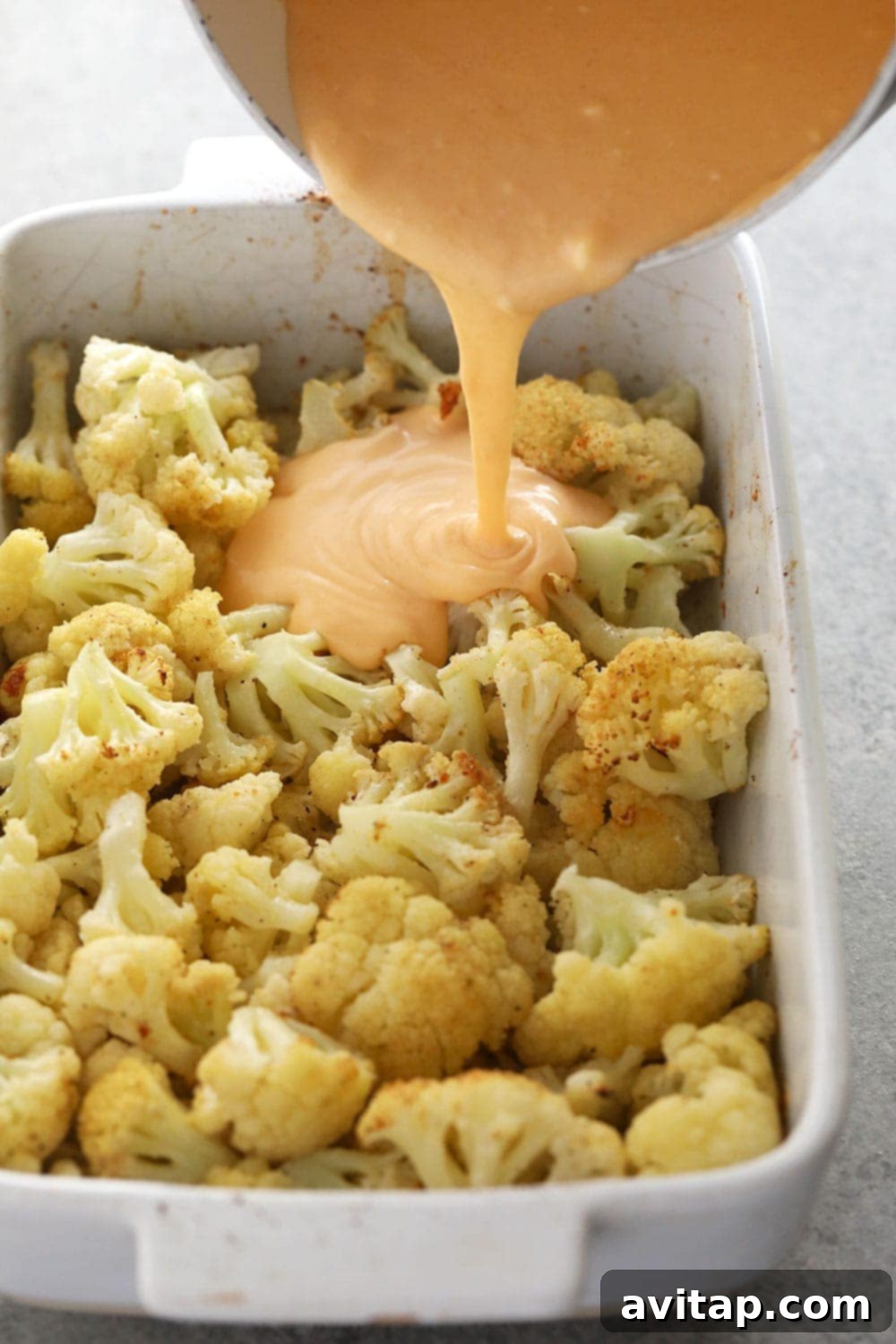 Ultimate Triple Cheese Cauliflower Mac 4 Delicious cheese sauce being generously poured over a bed of roasted cauliflower florets in a baking dish.