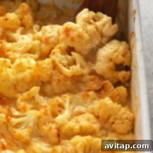 Ultimate Triple Cheese Cauliflower Mac 6 Cheesy cauliflower mac and cheese casserole in a baking dish with a wooden spoon, ready to serve.