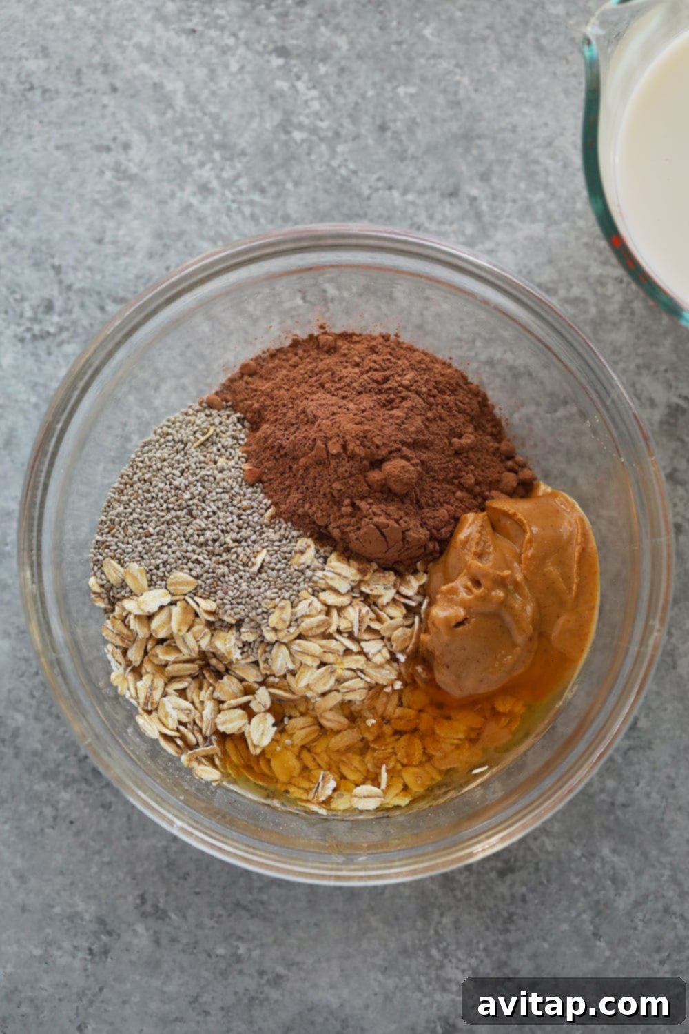 Overnight Oats Ingredients Individual ingredients for Chocolate Peanut Butter Overnight Oats laid out in separate bowls: oats, cocoa powder, chia seeds, peanut butter, almond milk, and honey.