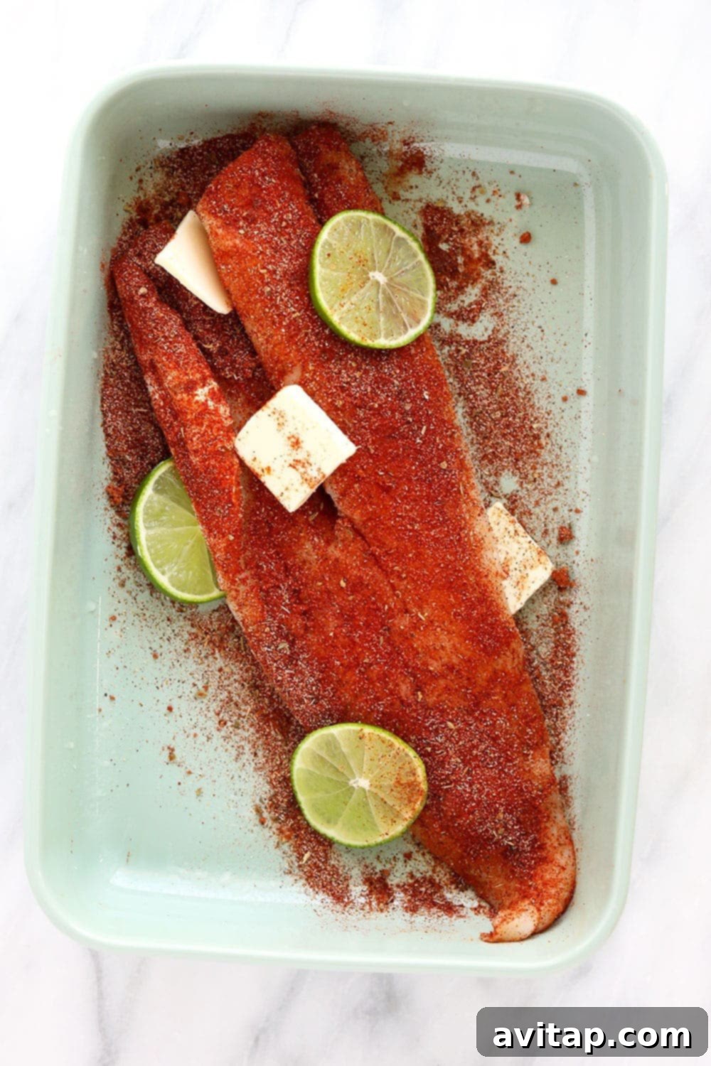 A pristine cod fillet seasoned and ready for baking in a glass dish.