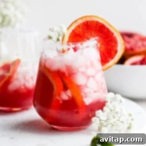 Two glasses of Blood Orange Margarita on a white plate, garnished with orange slices and salt.