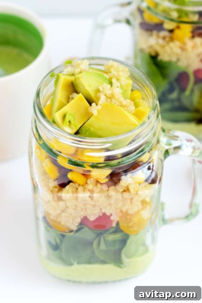 Mason jar salad held in hand, with fresh avocado slices on top, ready to eat.