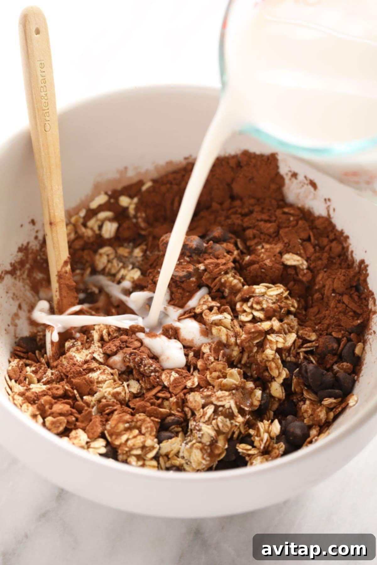 Cool Mint Chocolate Overnight Oats 2 Close-up shot of dry ingredients – rolled oats and cocoa powder – being mixed with a splash of almond milk in a clear bowl, illustrating the initial steps of preparing overnight oats.