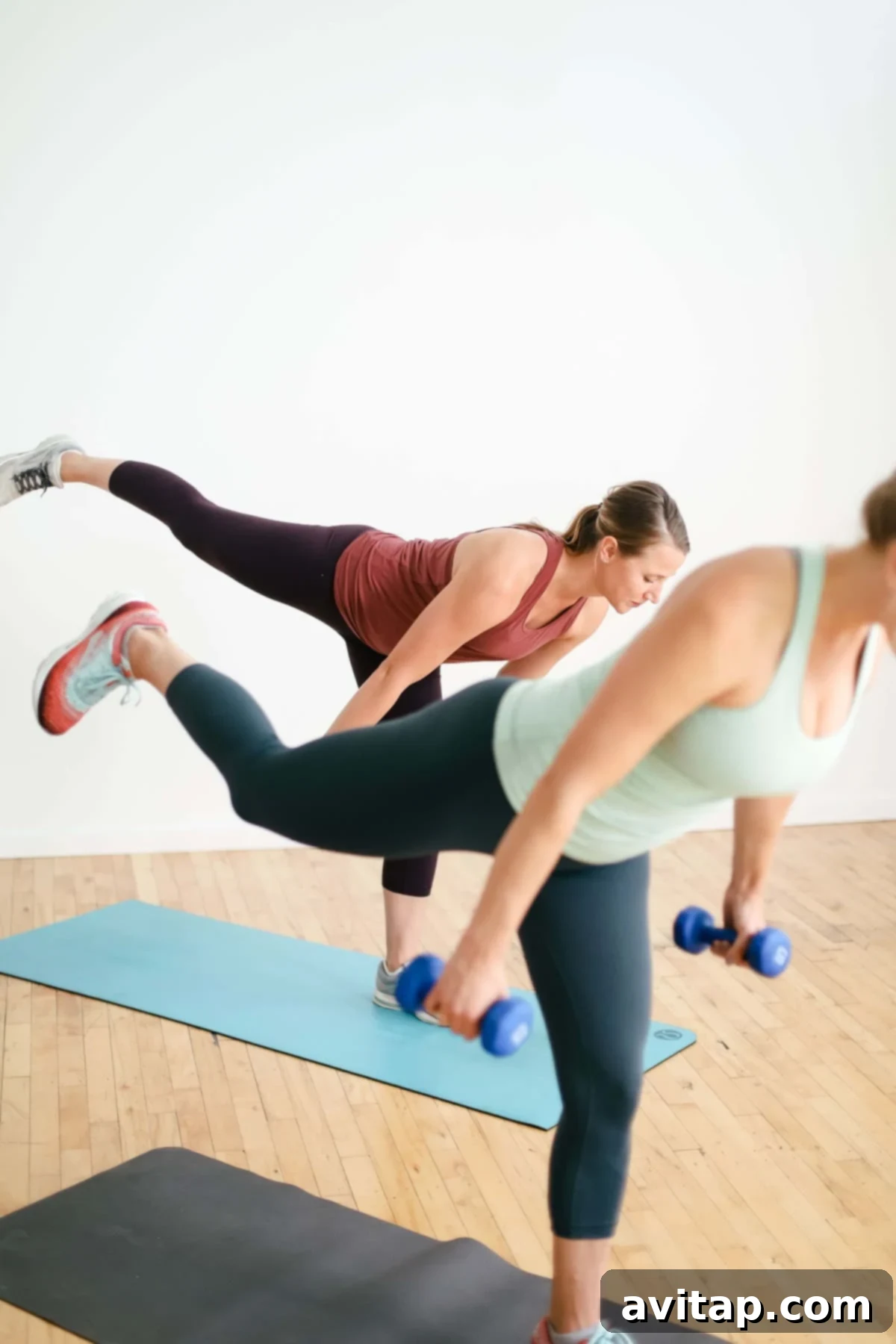 Two women engaged in a dynamic leg and glute workout in a modern fitness setting.