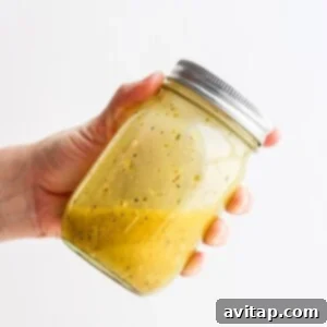 A hand holding a jar of Greek salad dressing.