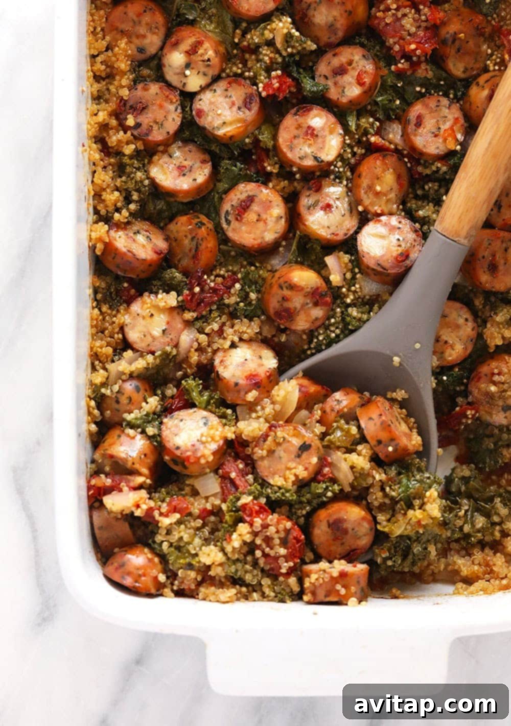 Italian Chicken Sausage Quinoa Casserole served in a dish with a large serving spoon, ready to be enjoyed.
