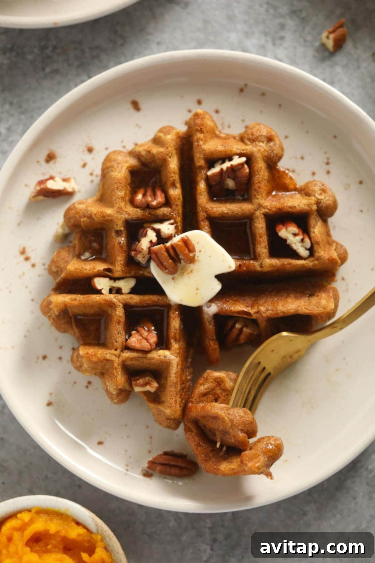 A delicious gluten-free pumpkin waffle on a plate with a fork, ready to be eaten.