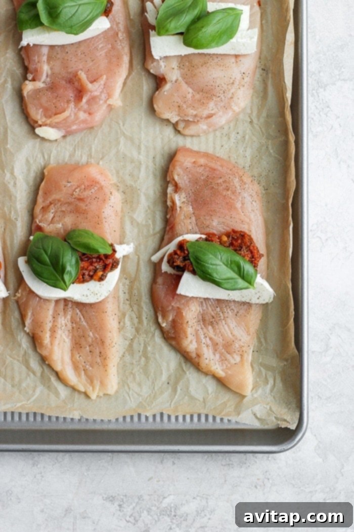 Caprese stuffed chicken breast laid open on a baking tray, showing mozzarella, basil, and sun-dried tomatoes inside.