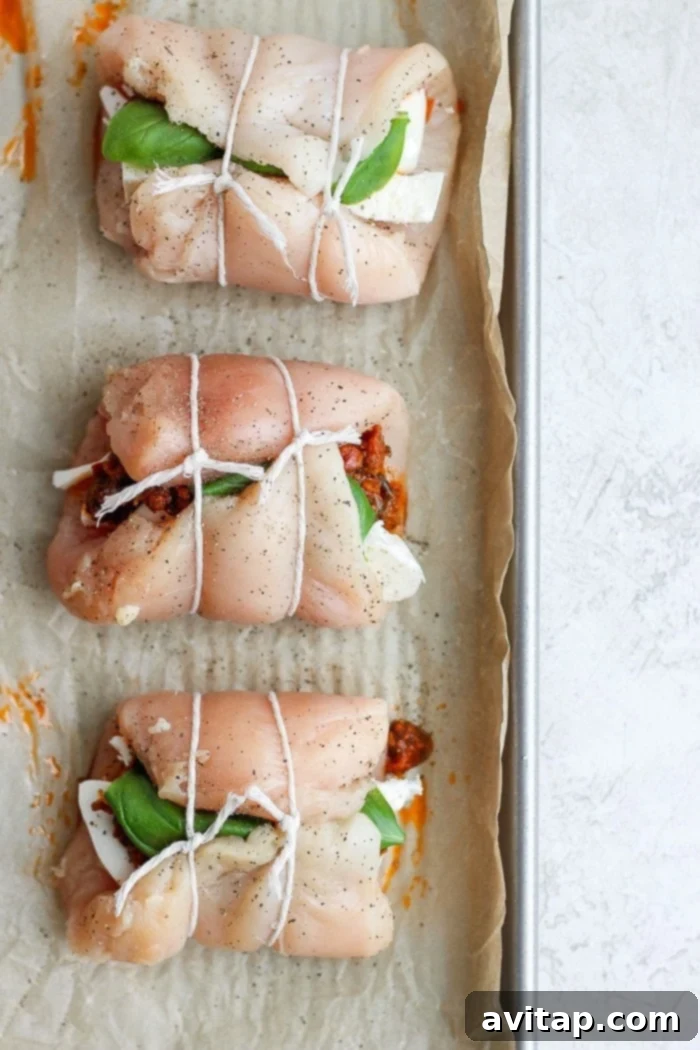 Caprese stuffed chicken breasts, rolled and tied with cooking twine, placed on a baking tray.