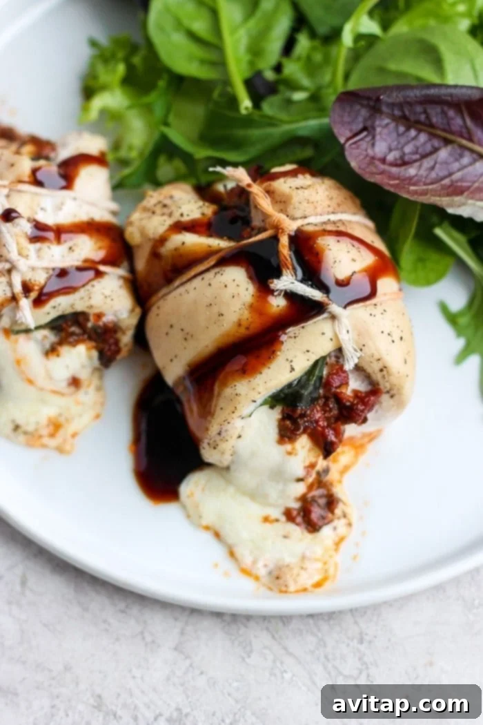 A serving of Caprese stuffed chicken breast with a side of fresh greens, drizzled with balsamic glaze.