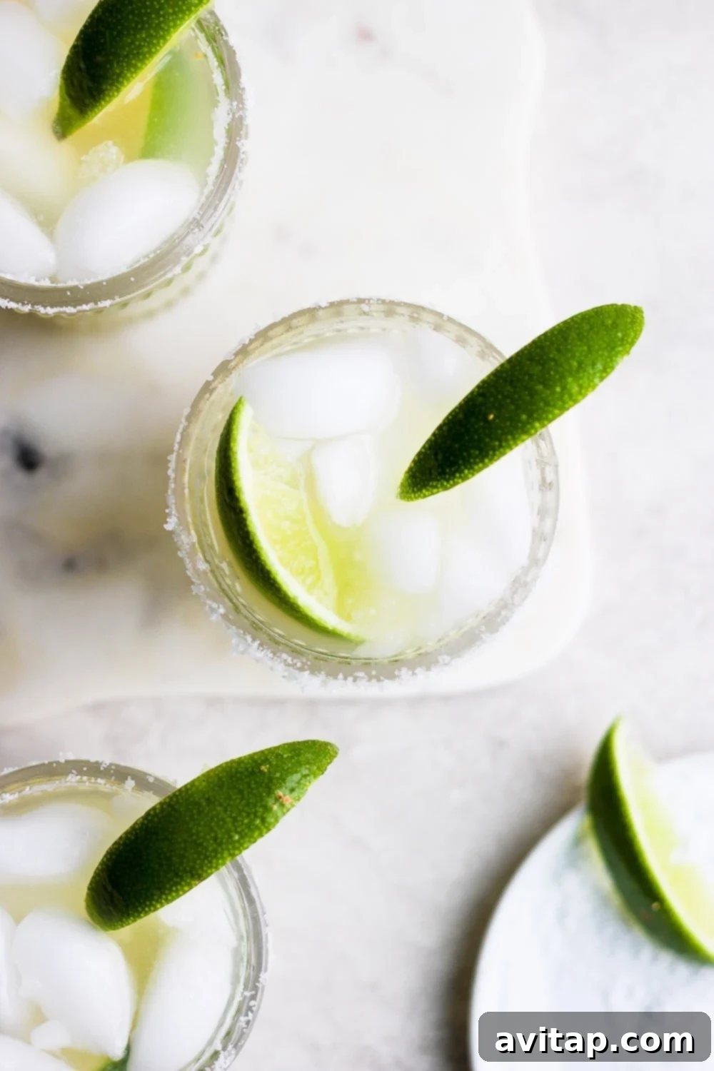 A close-up of two skinny margaritas in glasses, garnished with lime wedges and a salted rim.