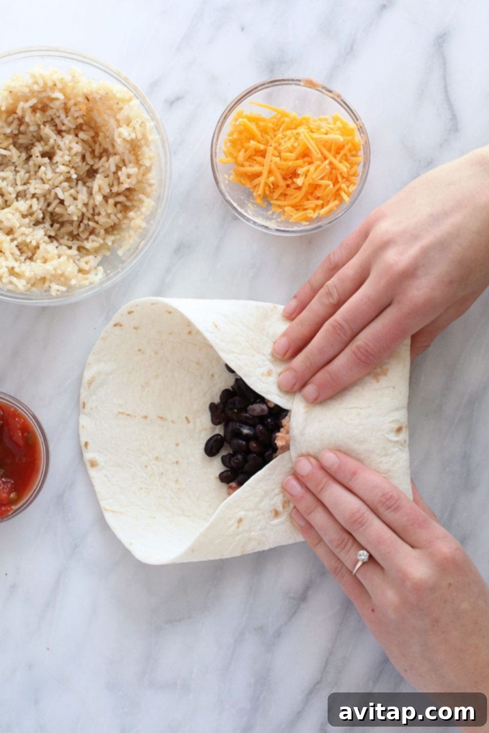 Simple 6-Ingredient Bean Burritos 5 A person wrapping a homemade bean and cheese burrito tightly in a flour tortilla, preparing it for cooking or freezing.