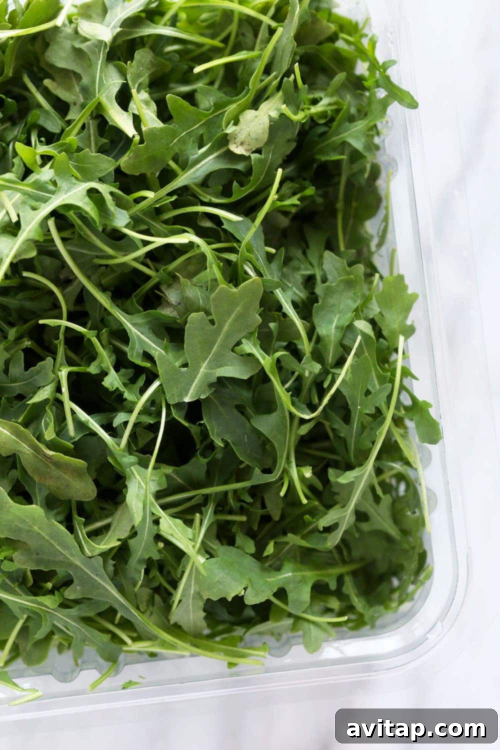 Fresh arugula leaves in a clear plastic container, ready for use.