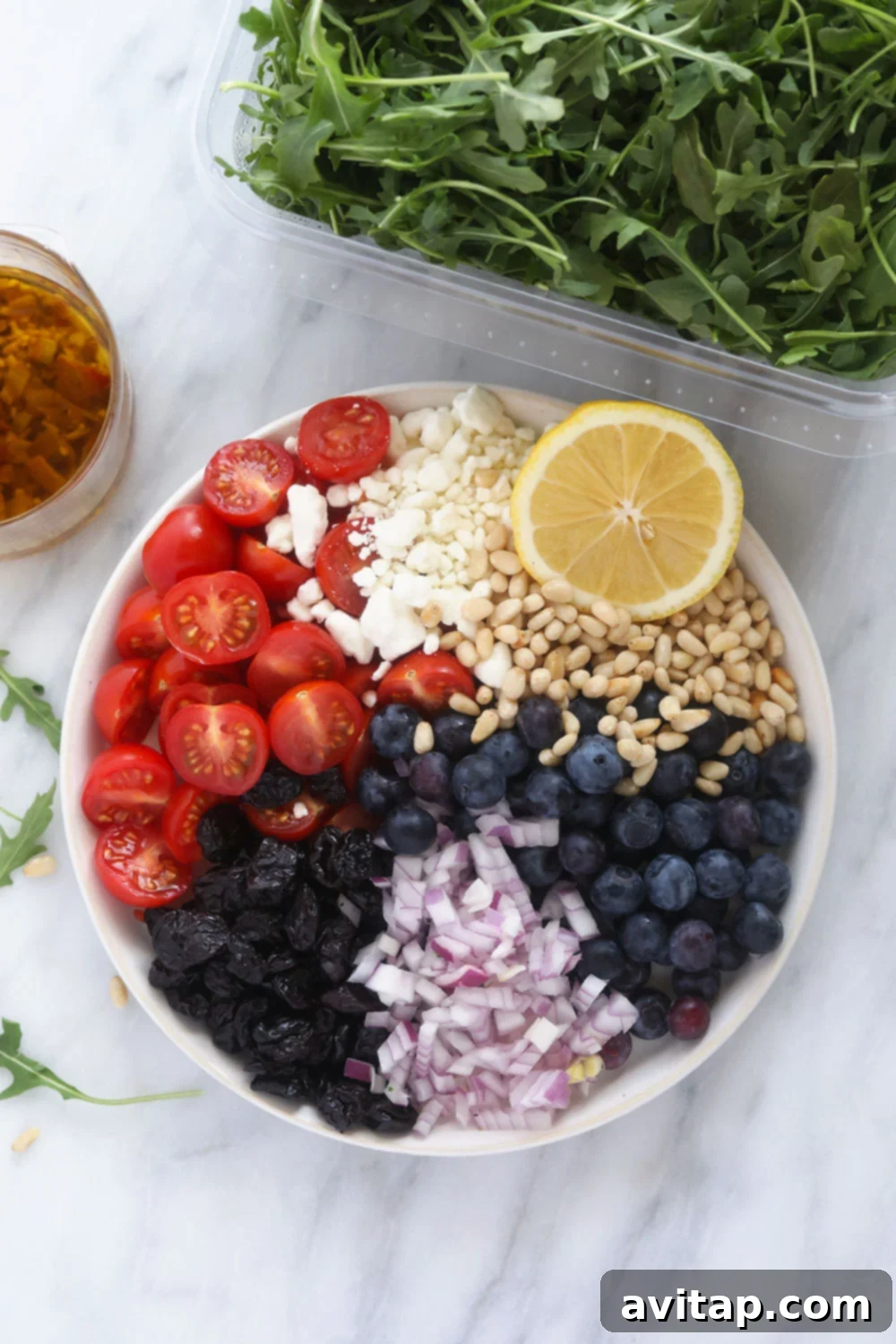 All the vibrant ingredients for the arugula salad neatly arranged on a white plate before mixing.