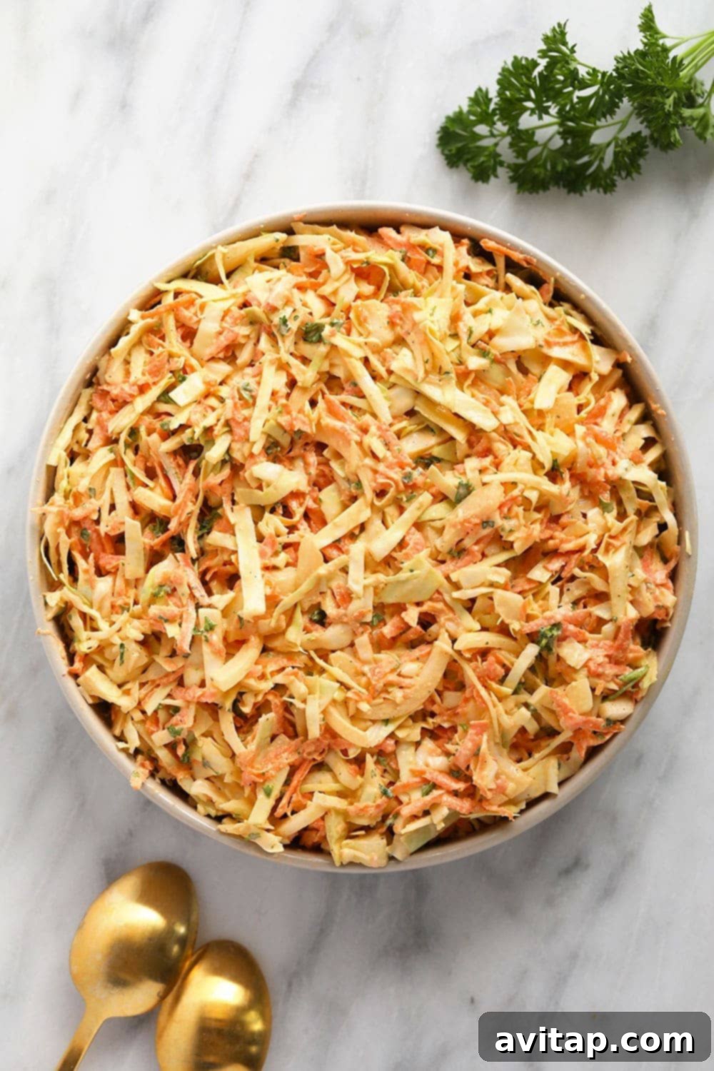 A large bowl of vibrant, creamy coleslaw, freshly prepared and garnished with parsley, ready to be served at a summer BBQ. The texture of the shredded cabbage and carrots is clearly visible.