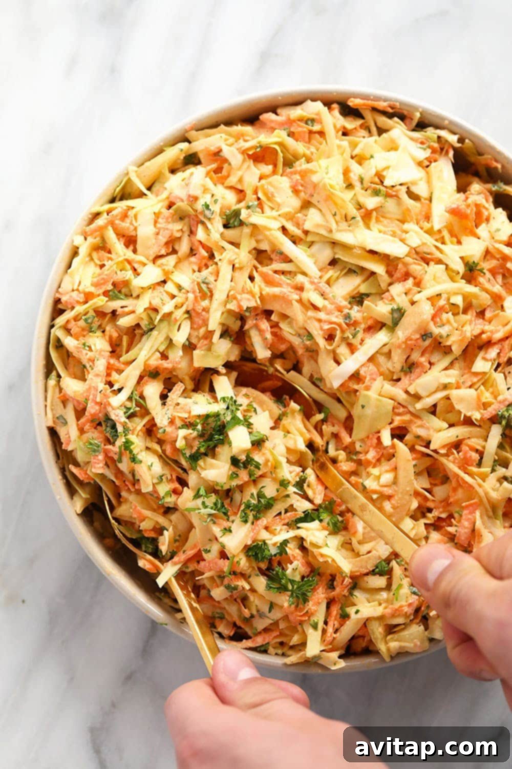 A close-up shot of creamy coleslaw in a elegant serving bowl, with two serving spoons scooping out a generous portion. The rich dressing and fresh vegetable shreds are clearly visible, inviting a taste.