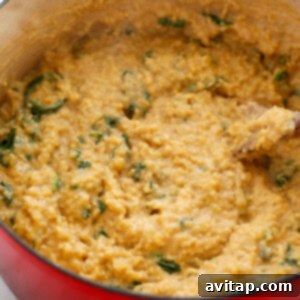 A red pan with a spoon and spinach in it.