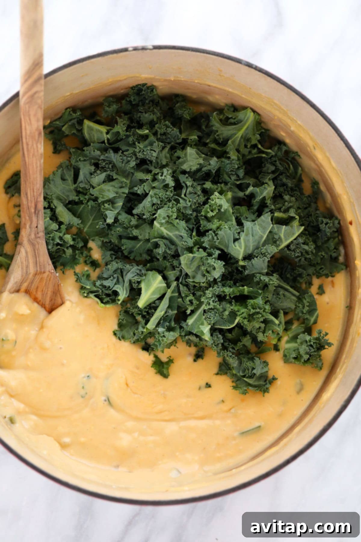 cheese sauce with fresh kale added in, ready to be mixed together for quinoa mac and cheese