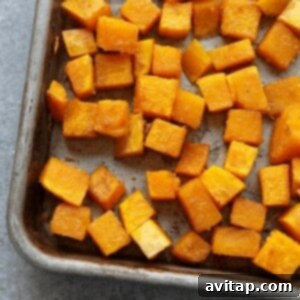 Cubed butternut squash seasoned on a baking pan, ready for roasting.
